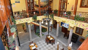 Un hall de hotel de varios niveles con barandillas ornamentales, piso a cuadros y un árbol de Navidad.