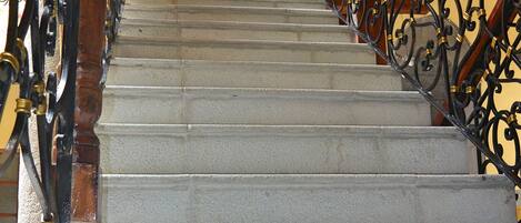 Una escalera con barandillas de metal ornamentadas y un pasamanos de madera, que lleva a una puerta en la parte superior.