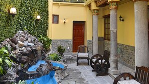 Un patio con fuente, mobiliario, un mural y un balcón con barandilla de hierro forjado.
