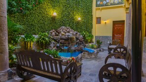 Un patio con una cascada de rocas, bancos y un muro cubierto de vegetación.