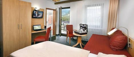 A hotel room with a bed, a desk with a computer, a chair, a wardrobe, and a window with curtains.