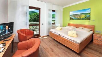 Habitación de hotel moderna con una cama grande, un escritorio con televisor, una silla y un balcón con vistas panorámicas.