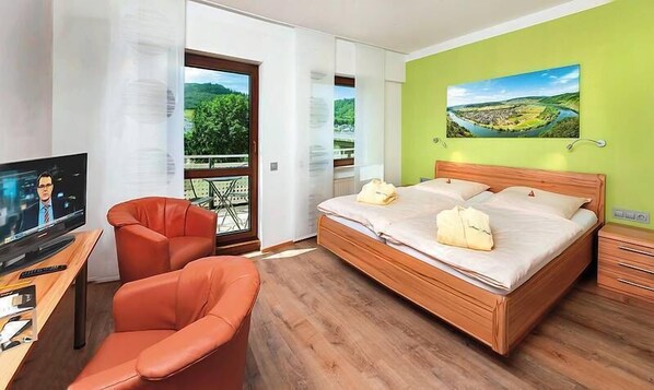 Habitación de hotel moderna con una cama grande, un escritorio con televisor, una silla y un balcón con vistas panorámicas.