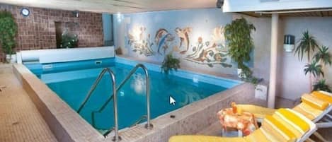 An indoor swimming pool with a tiled floor, a mural on the wall, and yellow lounge chairs.