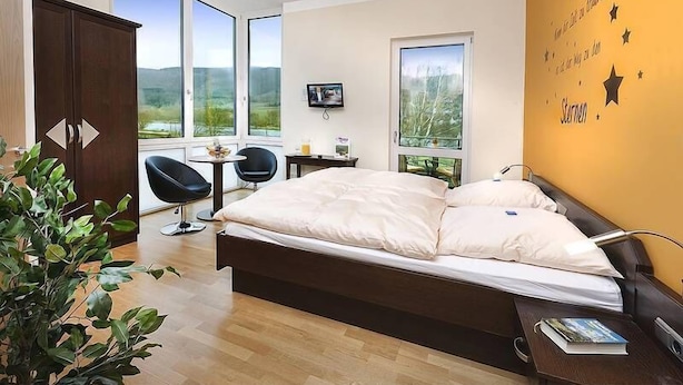 A bedroom with a bed, a desk, a chair, and large windows. - Hotel Pohl zum Rosenberg (Kinheim)