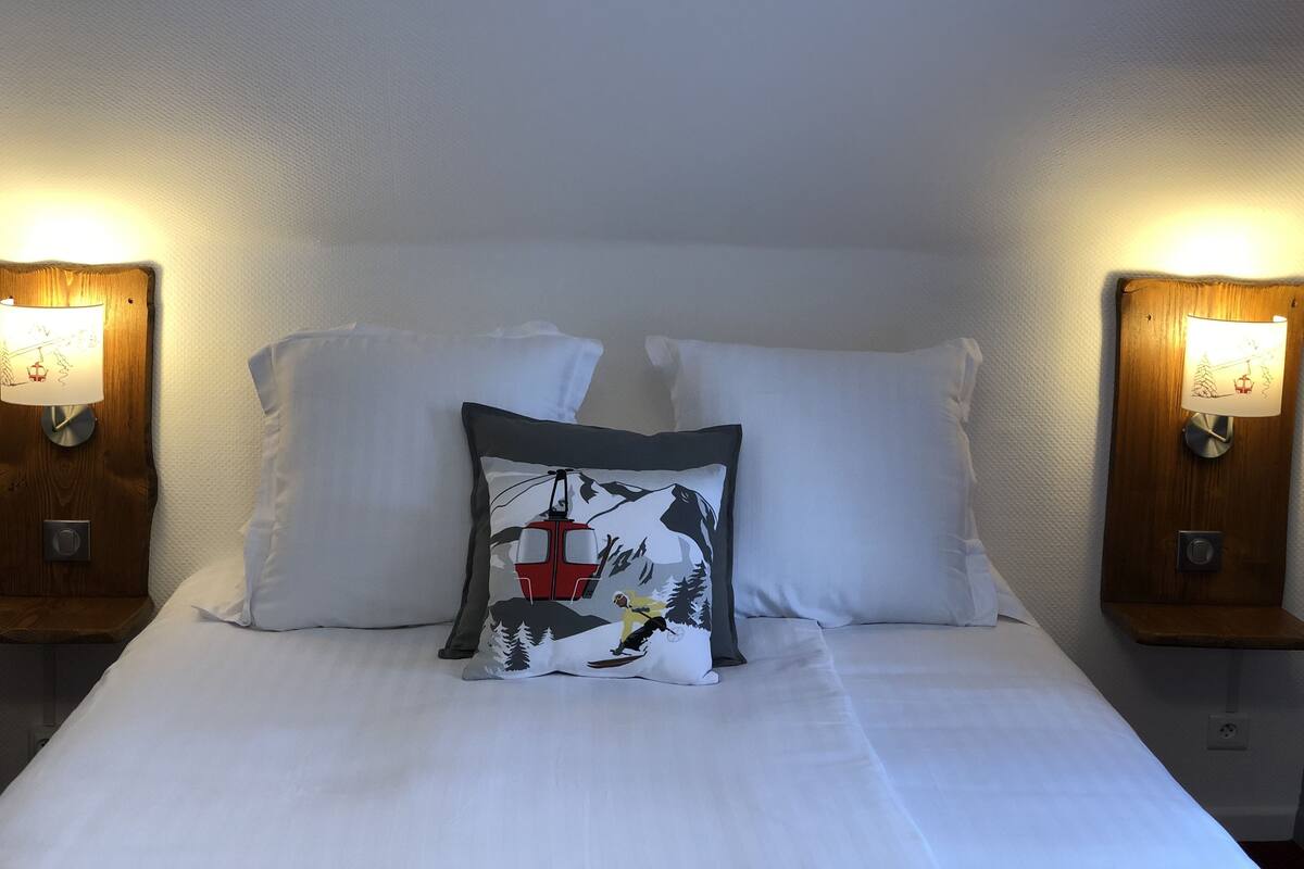 A bed with white linens, two white pillows, and a decorative pillow with a mountain scene.
