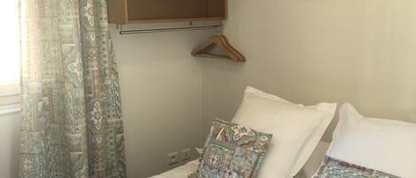 A neatly made bed with two pillows, a hanging wooden shelf, and a wall with a heart-shaped decoration.