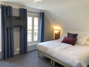 A bedroom with a bed, a TV mounted on the wall, a window with curtains, and a nightstand with a lamp. - Hôtel Génépi (Beuil)