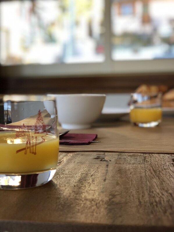 A wooden table with a glass of orange juice, a white bowl, and a napkin. - Hôtel Génépi (Beuil)