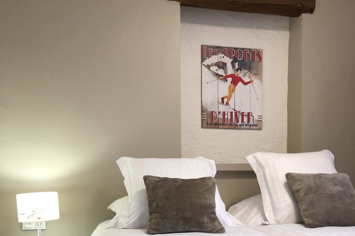 A neatly made bed with white linens and two pillows, a small bedside table with a lamp, and a poster on the wall.