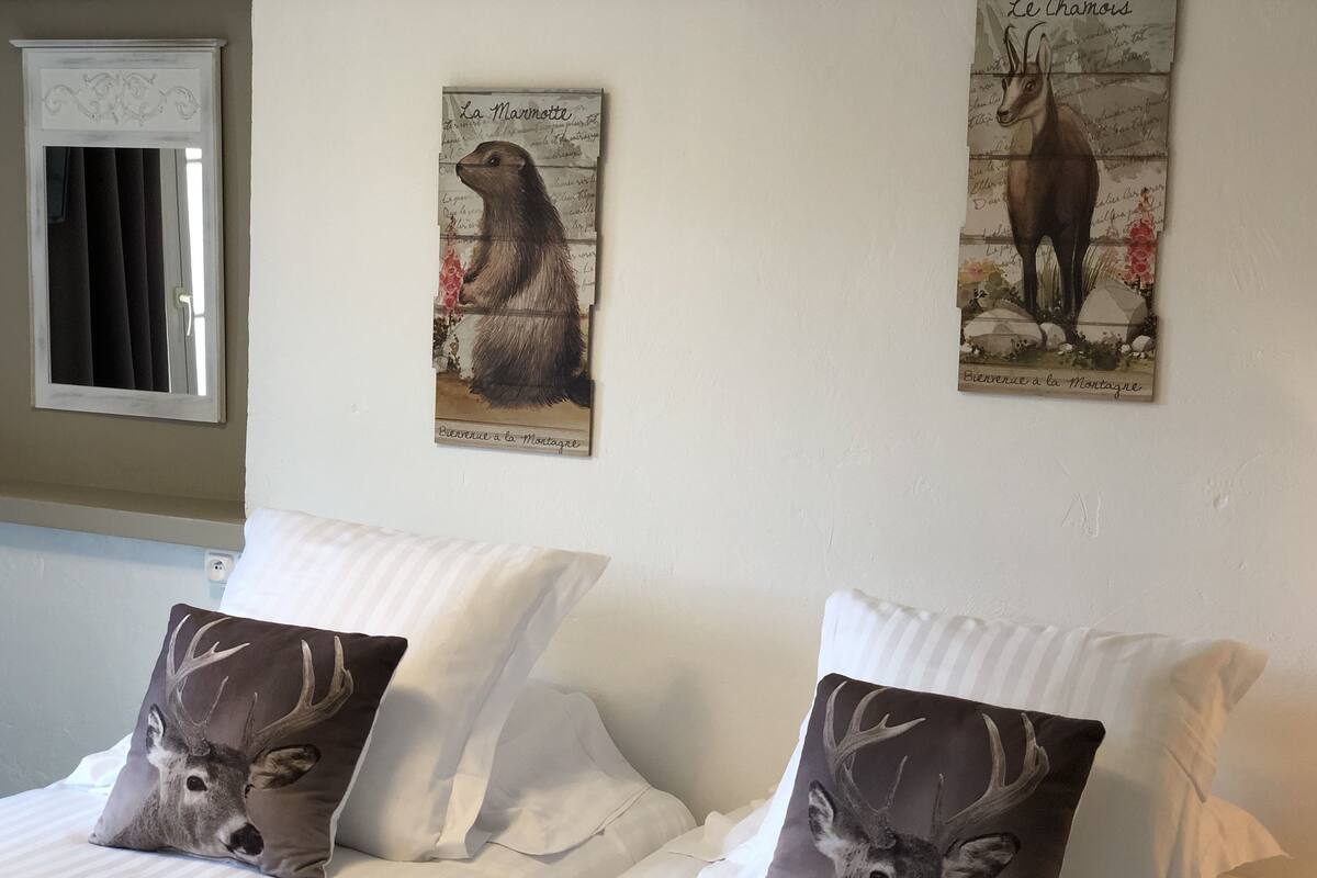 A hotel room with two beds, each with a pillow featuring a deer. There are two wall-mounted artworks depicting animals, one of a marmot and the other of a deer.