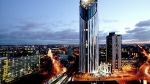 Un grattacielo moderno e imponente, con un design originale sulla sommità, immerso in una vivace area urbana con strade e altri edifici.