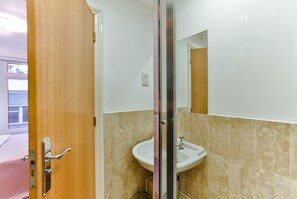 A bathroom with a wooden door, a glass shower enclosure, and a white sink.