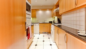 A modern kitchen with wooden cabinets, a dishwasher, a washing machine, and a countertop with a kettle and cups. - Theatreland Walk (London)