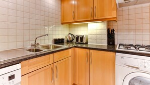 A kitchen with wooden cabinets, a stainless steel sink, a built-in oven, and a washing machine. - Theatreland Walk (London)