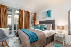 A modern bedroom with a large bed, a bedside table, a chair, and a window with curtains.