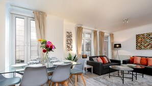 A modern living room with a glass dining table, grey chairs, a black sofa, and a coffee table. - Theatreland Walk (London)