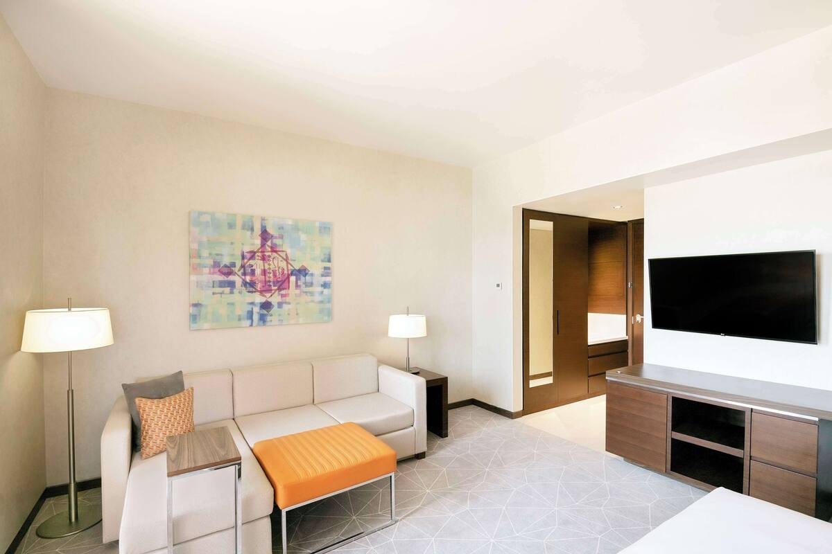 Ein modernes Hotelzimmer mit einer Couch, einem Couchtisch, einem Flachbildfernseher und einem Gemälde an der Wand.