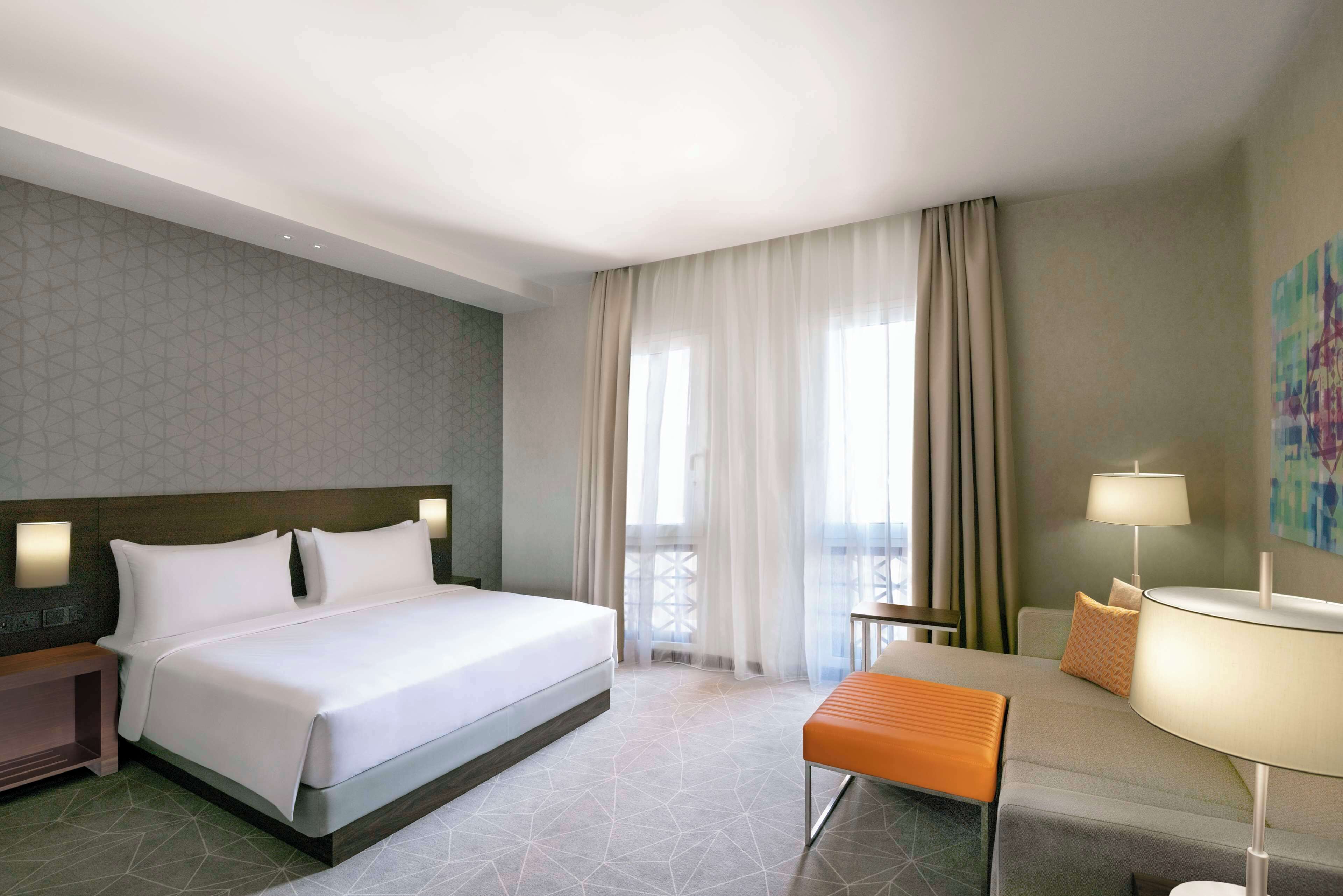 Une chambre d’hôtel avec un grand lit, une table de chevet, une chaise, un canapé et une fenêtre avec des rideaux.