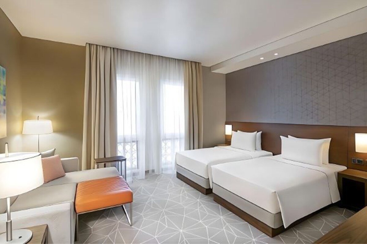 Een hotelkamer met twee bedden, een bureau, een stoel, een klein tafeltje en een raam met gordijnen.