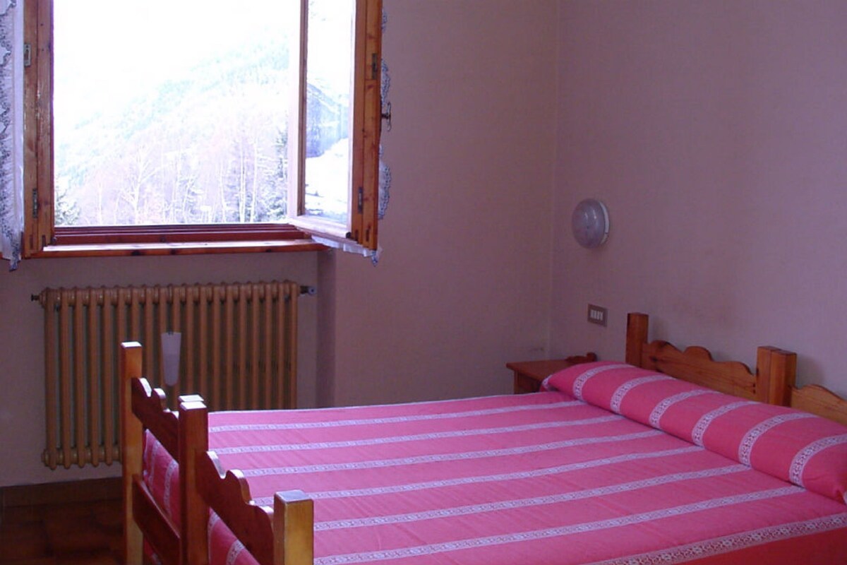 A bedroom with a wooden bed, a window with a view of trees, and a radiator.