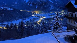 Un paysage montagneux enneigé, avec un village illuminé dans la vallée et un bâtiment doté d’un toit très pentu.