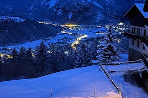 A snow-covered mountain landscape with a lit village in the valley and a building with a steep roof. - Hotel Ginepro (Valdisotto)