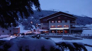 Un immeuble à plusieurs étages abritant un cinéma et un restaurant au rez-de-chaussée, entouré d’arbres et de montagnes enneigés.