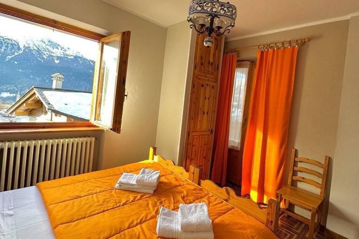 Habitación de hotel con una cama, una silla de madera, un ventanal con vistas a montañas y un radiador.