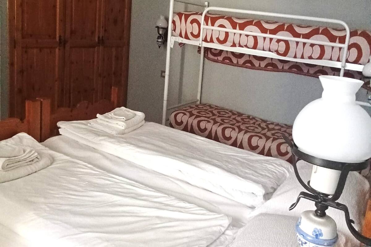 Una habitación con dos literas, una con cubrecama estampado y la otra con cubrecama blanco liso. Hay una lámpara blanca sobre una mesita de noche.