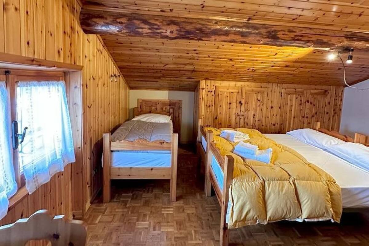 Habitación de cabaña de madera con dos camas, suelo de madera y techo con vigas a la vista.