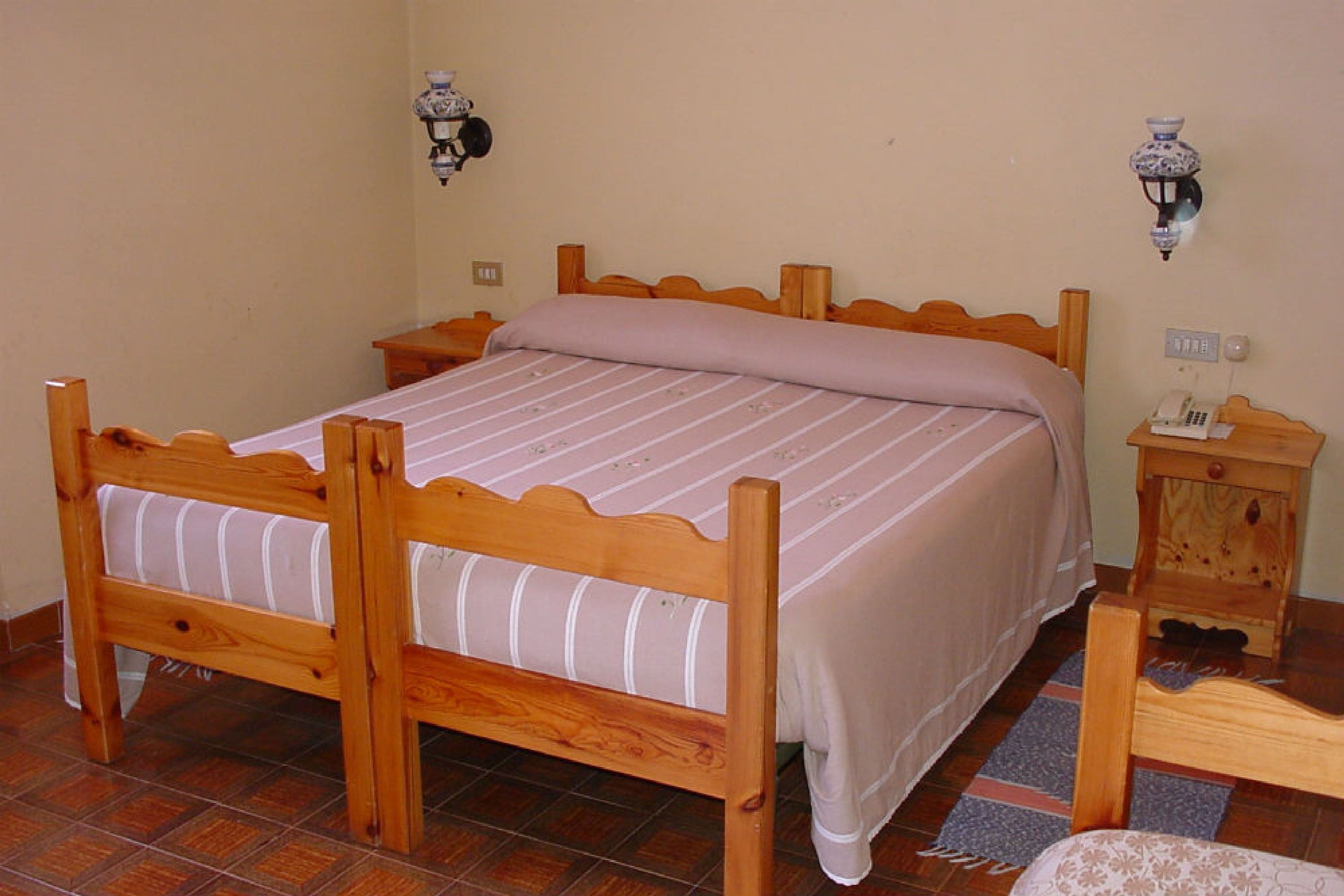 A wooden bed with a striped bedspread, a bedside table with a lamp, and a small wooden cabinet.