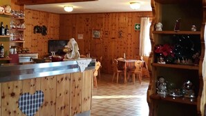 Puinen sisustus, jossa on keittiöalue. Keittiöön kuuluu muun muassa sydämenmuotoisia aukkoja sisältävä työtaso, ruokapöytä ja koriste-esineillä varustettu hylly.