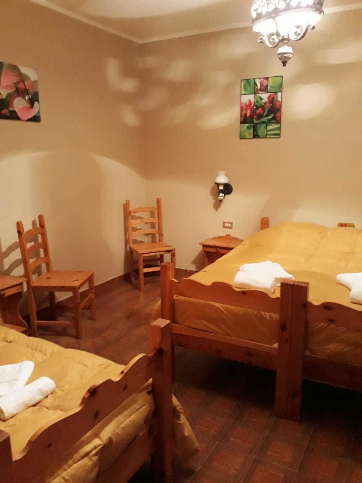 A cozy room with two wooden beds, a wooden chair, a small table, and a wall-mounted lamp.