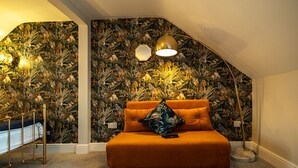 A bedroom with a sloped ceiling, a bed with orange bedding, a decorative pillow, and a wall with a jungle-themed wallpaper. - Channel View Guest House (Weymouth)