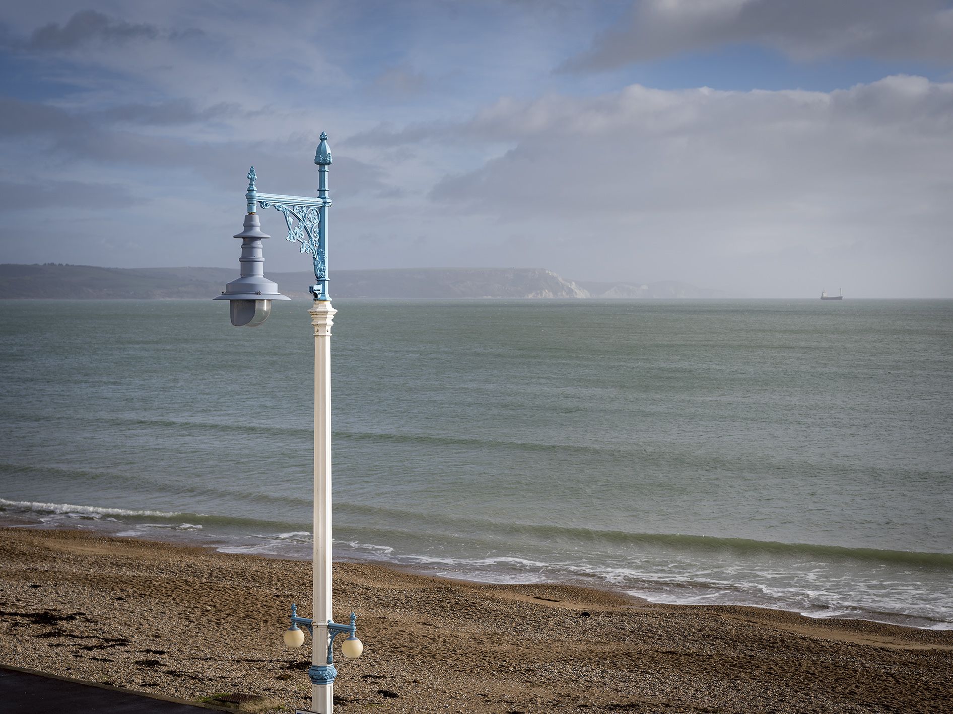 A coastal scene with a white lamp post and a ship in the distance.