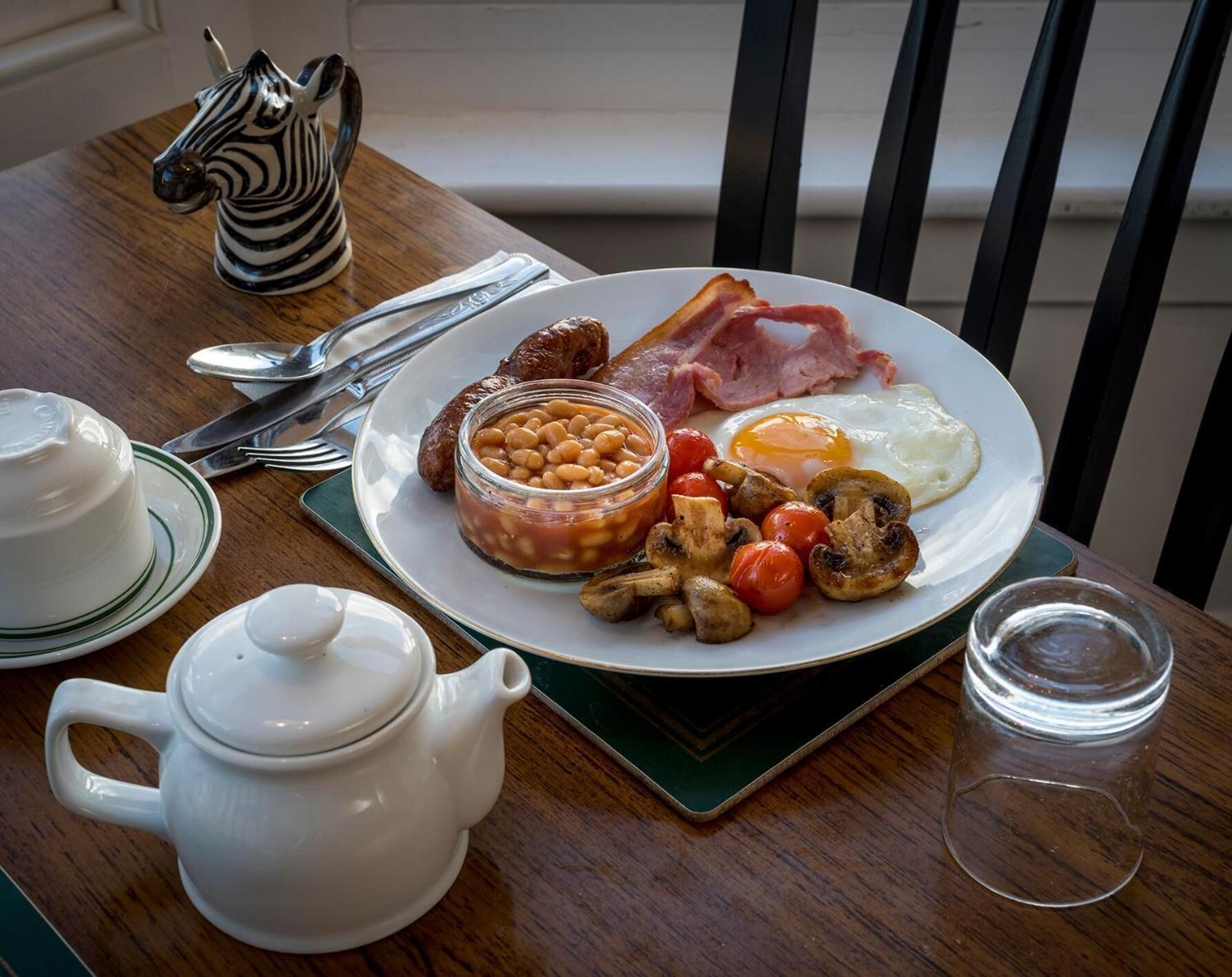 A breakfast plate with eggs, bacon, sausages, beans, tomatoes, and mushrooms.