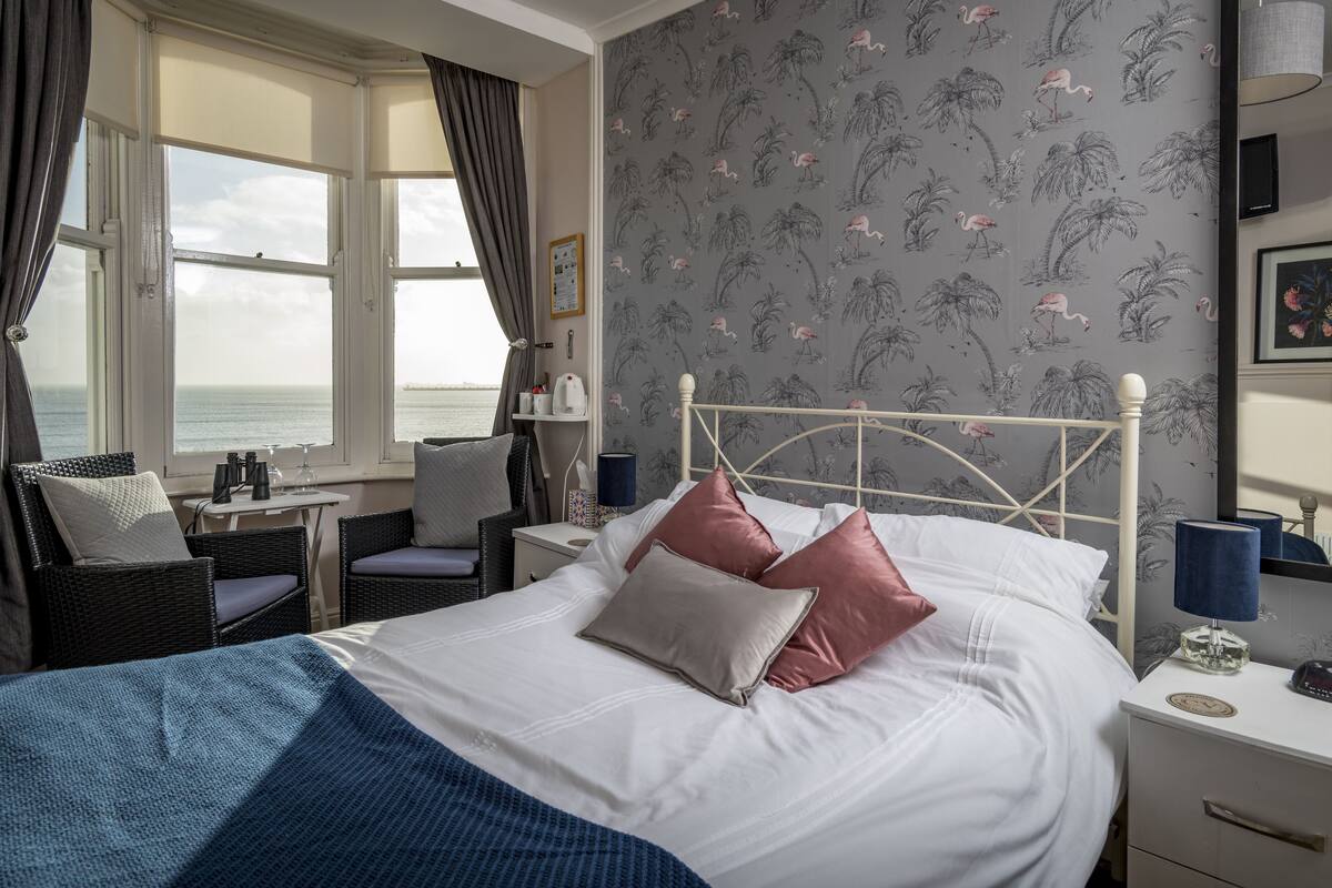 Ein Schlafzimmer mit Bett, Schreibtisch und Stuhl am Fenster mit Meerblick.