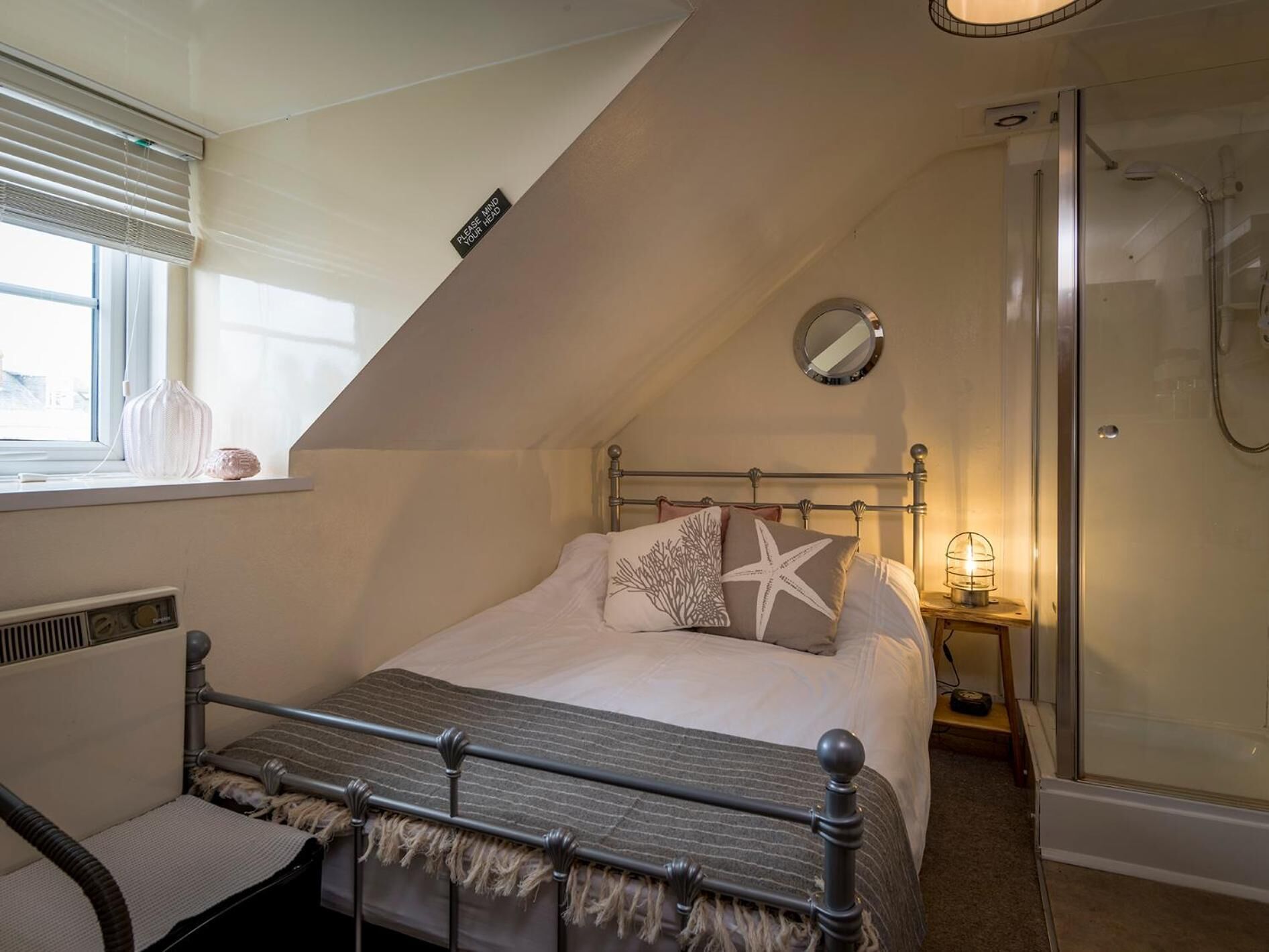A bedroom with a bed, a bedside table, a mirror, and a shower.