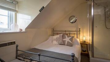 A bedroom with a bed, a bedside table, a mirror, and a shower.