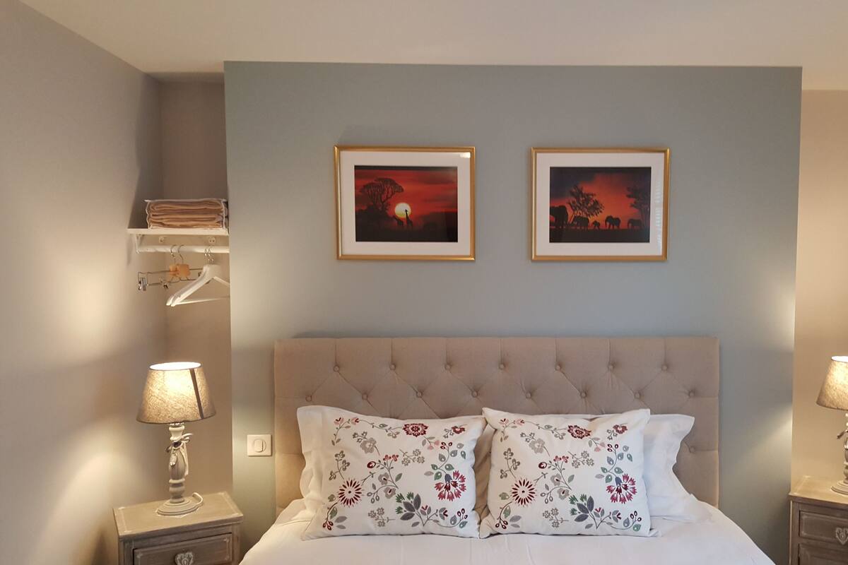 A bedroom with a tufted headboard, two floral pillows, two framed pictures on the wall, and bedside lamps.