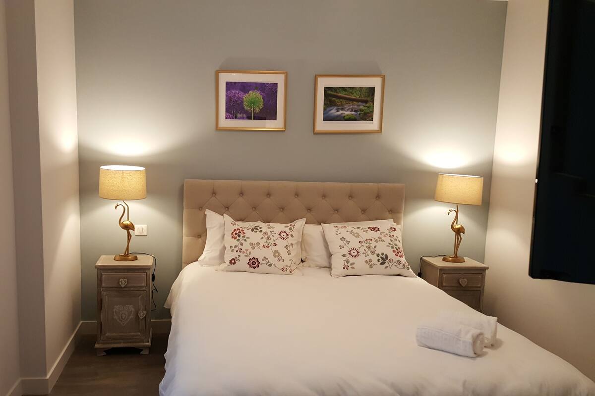 A neatly made bed with floral pillows, two bedside lamps, and two framed pictures on the wall.