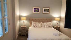 A neatly made bed with floral pillows, two bedside lamps, and two framed pictures on the wall. - Hôtel Linxa (Tours)