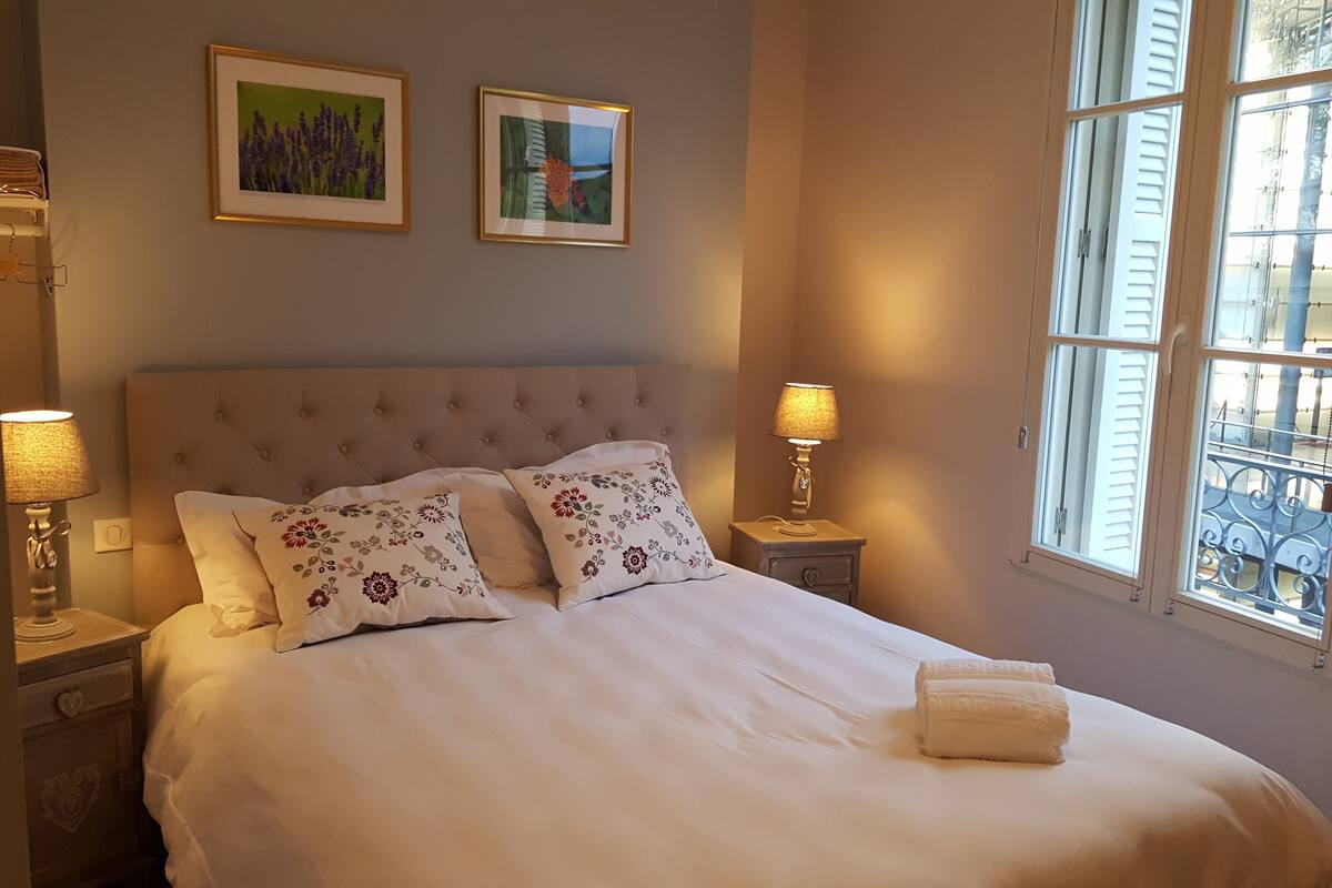 A neatly made bed with floral pillows, two bedside lamps, and a window with a view.