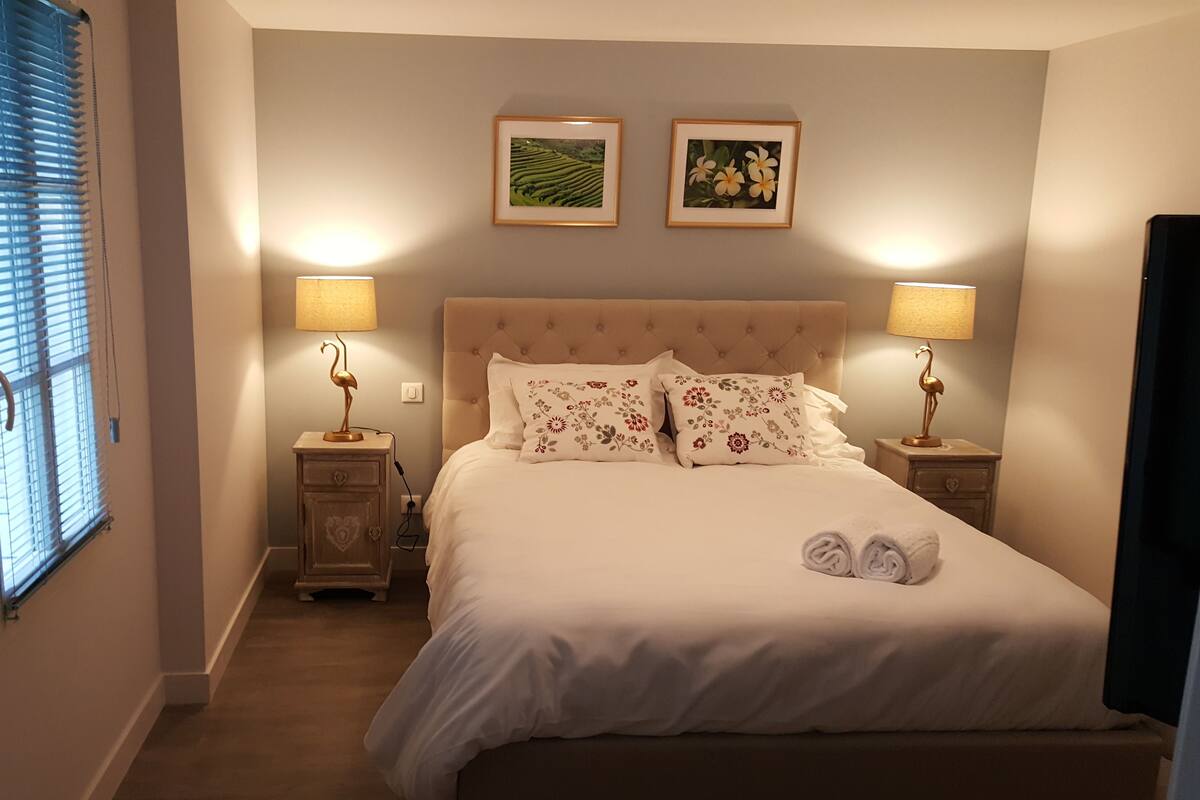 A neatly made bed with floral pillows, two bedside lamps, and two framed pictures on the wall.