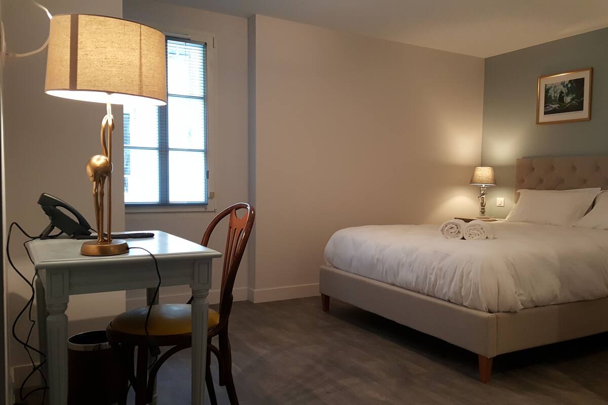 A bedroom with a bed, a desk with a lamp, a chair, and a window.