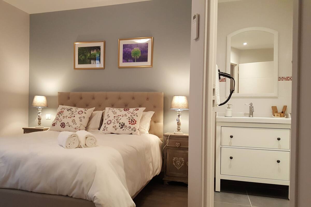 A bedroom with a large bed, two nightstands with lamps, a dresser, and a bathroom visible through an open door.