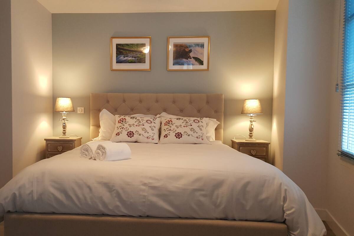 A neatly made bed with floral pillows, two bedside lamps, and framed pictures on the wall.