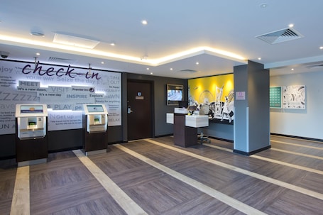 A hotel reception area with a check-in counter, self-service machines, and a wall with motivational phrases.. Premier Inn Gloucester - Quayside