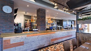 A modern bar area with a wooden counter, seating, and a hexagonal patterned floor. - Premier Inn Gloucester - Quayside (Gloucester)